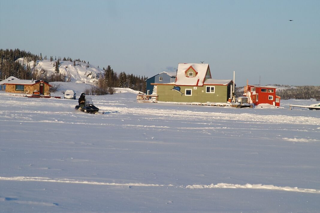 Northwest Territories Travel Guide 2026: Yellowknife, Aurora Borealis, and the Wilderness North Colourful houseboats frozen into the ice of Great Slave Lake at Yellowknife with a snowmobiler crossing, Northwest Territories