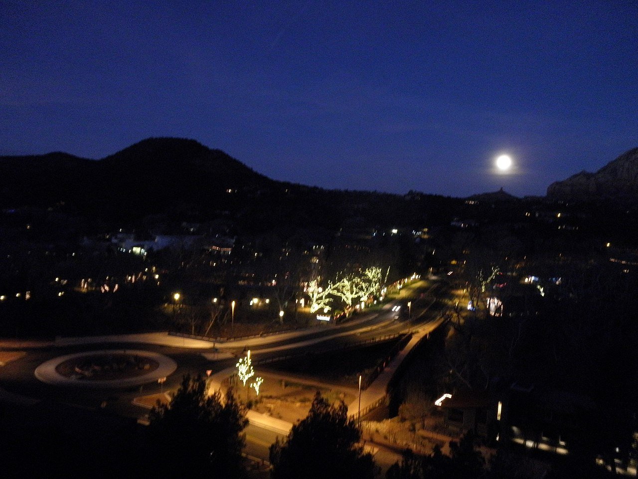 Full moon rising over Sedona Arizona with city lights and red rock silhouettes at night