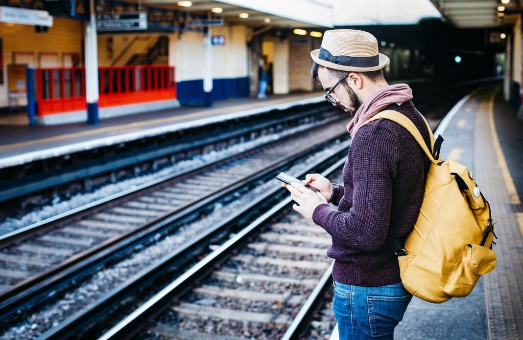 How to Travel on a Budget: 11 Proven Strategies That Actually Work Solo backpacker with yellow backpack checking phone at train station platform budget travel