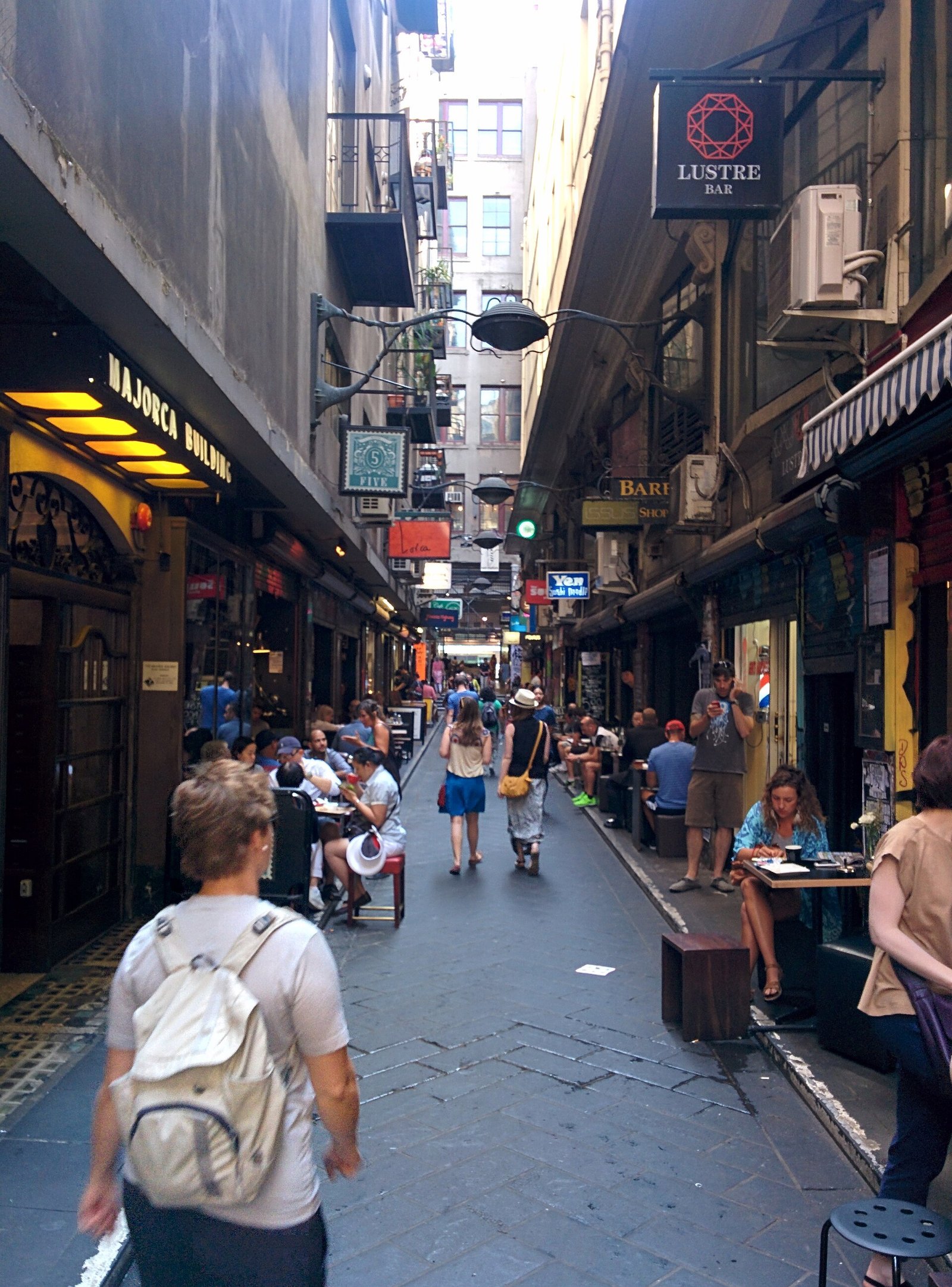 Degraves Street coffee laneway in Melbourne's CBD lined with café signage and crowded with outdoor dining tables beneath the hanging shopfront signs